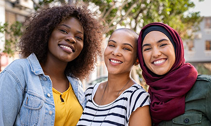 A multiracial group of woman are standing together, and smiling.