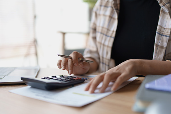 Person using calculator and holding a pen while referencing tax sheet.